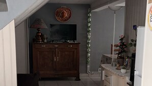 A narrow hallway with a dining table and chairs on the left, a wooden cabinet with a television in the center, and a refrigerator on the right. - Logement très spacieux.portail un code digital.bte à clé. Animals refused. (Dangé-Saint-Romain)