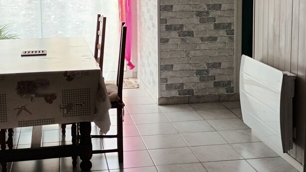 A dining area with a table and chairs, a brick wall, and a window with curtains. - Logement très spacieux.portail un code digital.bte à clé. Animals refused. (Dangé-Saint-Romain)