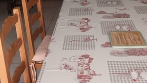 A dining area with a table set for two, a wooden chair, a sofa with patterned cushions, and a red bed in the background. - Logement très spacieux.portail un code digital.bte à clé. Animals refused. (Dangé-Saint-Romain)