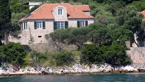 Ein Steinhaus mit rotem Ziegeldach, grünen Fensterläden und Blick auf das Meer.