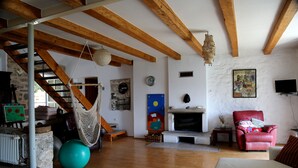 Ein geräumiges Wohnzimmer mit Holzbalken, einer Hängematte, einem Kamin, einem roten Sessel und einer Steinwand.