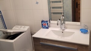 Un baño con lavadora blanca, un lavabo con espejo y un armario de madera.