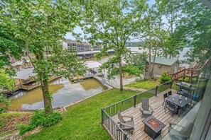 A deck with outdoor furniture, a small pond, and a view of a residential area with houses and a dock. - Lakefront Oasis w/ Private Dock + Paddle Boards (Lake Ozark)