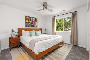 A bedroom with a bed, nightstands, a ceiling fan, a window with curtains, and a painting on the wall. - Lakefront Oasis w/ Private Dock + Paddle Boards (Lake Ozark)
