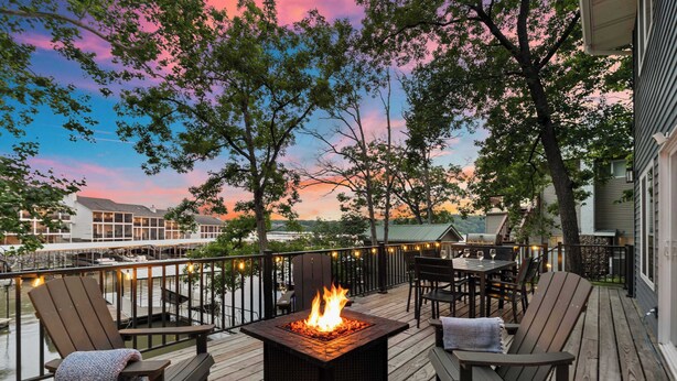 A deck with a fire pit, outdoor seating, and a view of a residential area. - Lakefront Oasis w/ Private Dock + Paddle Boards (Lake Ozark)
