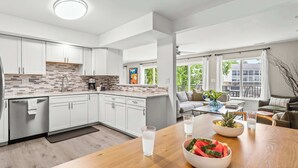 A modern kitchen with white cabinets, a tiled backsplash, and a dining area with a wooden table and chairs. - Lakefront Oasis w/ Private Dock + Paddle Boards (Lake Ozark)