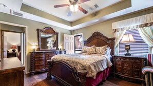 A bedroom with a large wooden bed, a ceiling fan, a dresser, and a mirror. - Casa de Capucine: Timeless Elegance & Grand Interiors. (Humble)