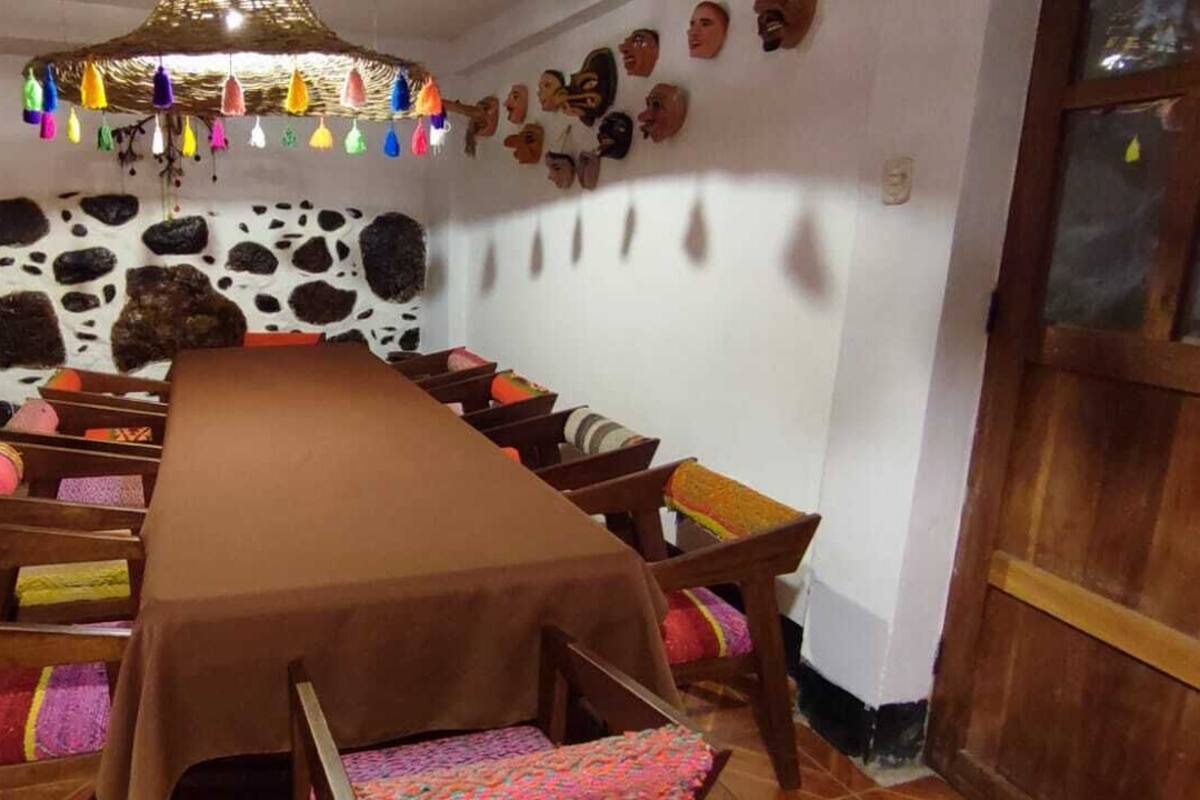Un comedor con una mesa larga, sillas, una lámpara decorativa colgante y una pared con estampado de vaca.
