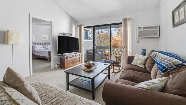 A living room with a sofa, coffee table, TV, and a balcony with a chair. - 2-bedroom condo at Ocean Edge with AC and comfort; Pool Access Available (Brewster)