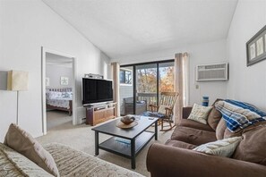 A living room with a sofa, coffee table, TV, and a balcony with a chair. - 2-bedroom condo at Ocean Edge with AC and comfort; Pool Access Available (Brewster)