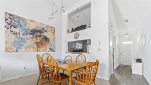 A dining area with a wooden table and chairs, a large abstract painting, and a kitchen area with a microwave and cabinets. - 2-bedroom condo at Ocean Edge with AC and comfort; Pool Access Available (Brewster)