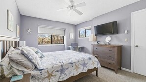 A bedroom with a bed, a ceiling fan, a dresser, a TV, and a window with blinds. - 2-bedroom condo at Ocean Edge with AC and comfort; Pool Access Available (Brewster)