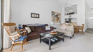 A living room with a brown sofa, a rocking chair, a coffee table, and a dining area with a table and chairs. - 2-bedroom condo at Ocean Edge with AC and comfort; Pool Access Available (Brewster)