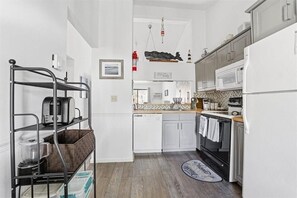 A modern kitchen with white cabinets, a black stove, and a dishwasher. There is a metal shelf unit with kitchen items on it. - 2-bedroom condo at Ocean Edge with AC and comfort; Pool Access Available (Brewster)