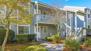 A two-story apartment building with a covered front porch, a staircase to the upper level, and a well-maintained lawn. - 2-bedroom condo at Ocean Edge with AC and comfort; Pool Access Available (Brewster)