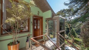 Uma casa com escadaria de madeira que dá para uma varanda, cercada por vegetação e um carro estacionado em frente.