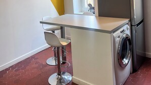 A compact kitchen with a built-in washing machine, a small dining area with two bar stools, and a modern ceiling light fixture. - Quiet apartment in the heart of the Cours Julien (Marseille)