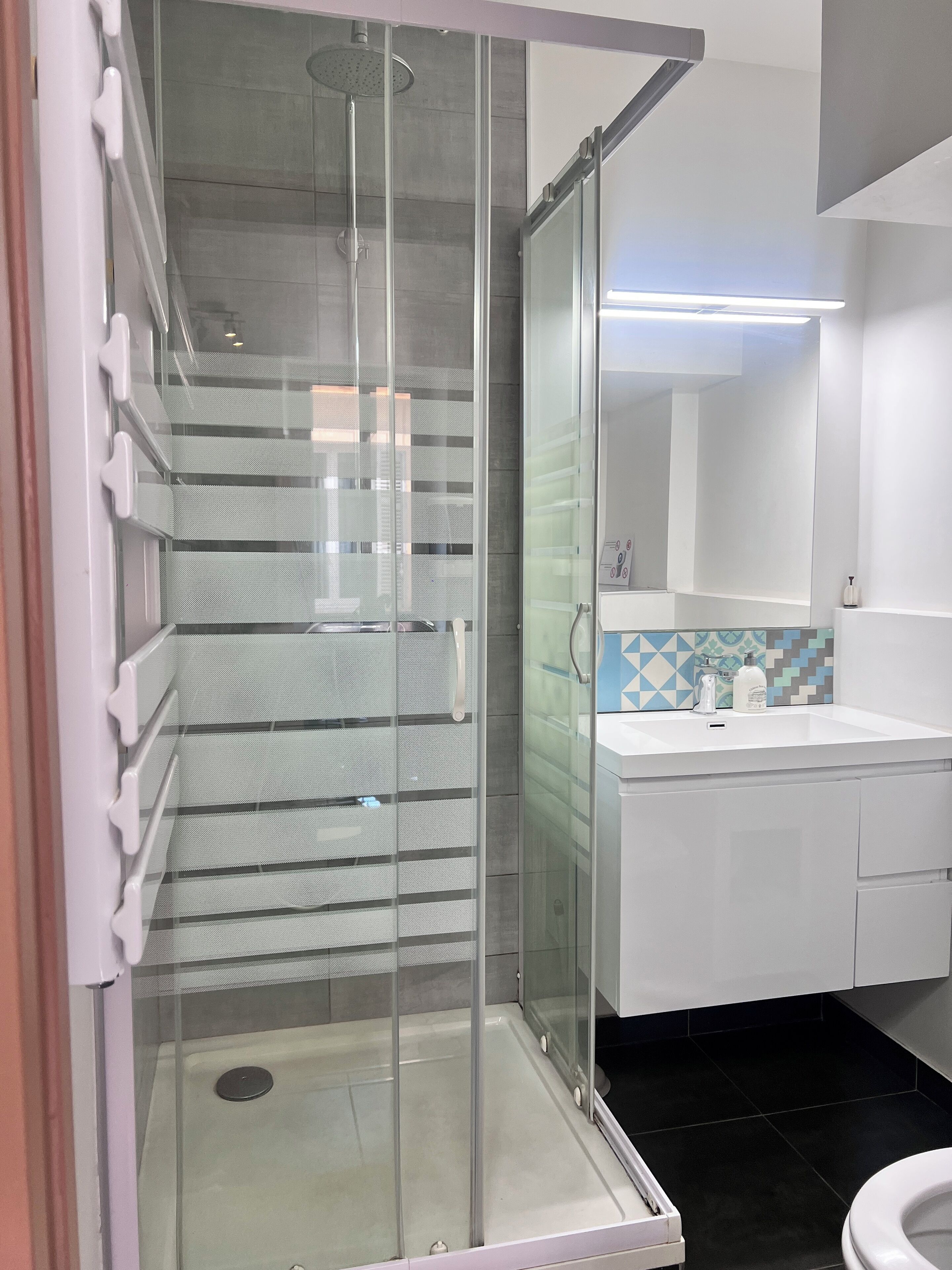 Une salle de bain moderne avec une douche à parois de verre, un lavabo blanc et un mur recouvert de carreaux.