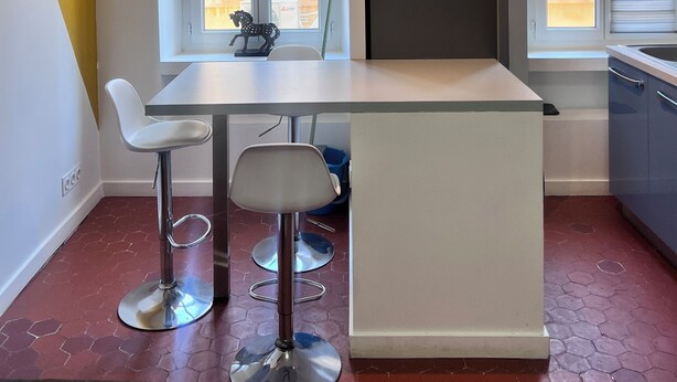 A compact kitchen with a central island, a dining area with two chairs, and a window with blinds. - Quiet apartment in the heart of the Cours Julien (Marseille)