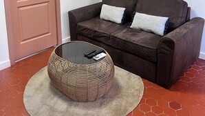 A room with a brown leather sofa, a round wicker coffee table, and a brown door. - Quiet apartment in the heart of the Cours Julien (Marseille)