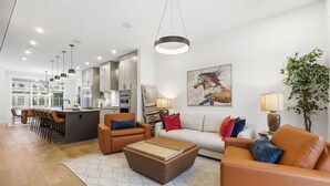 A modern living room with a sofa, coffee table, and chairs. There is a kitchen in the background with cabinets and a dining area. - Modern Home with Spa Bath & Garage Altadore (Calgary)