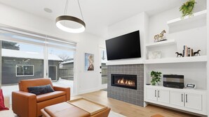 A modern living room with a fireplace, leather sofas, a flat-screen TV, and a bookshelf. - Modern Home with Spa Bath & Garage Altadore (Calgary)