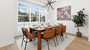 A dining area with a large window, a modern chandelier, and a painting on the wall. - Modern Home with Spa Bath & Garage Altadore (Calgary)