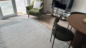 Een moderne woonkamer met een groene fauteuil, een houten eettafel en een flatscreen televisie.
