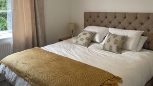 Een net opgemaakt bed met een gestoffeerd hoofdbord, witte lakens en gestreepte kussens.