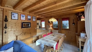 A wooden cabin interior with a dining table, chairs, a sofa, a kitchen area, and framed pictures on the walls. - Chalet, wifi, balcony, parking, tv, 90m², Les Gets (Les Gets)