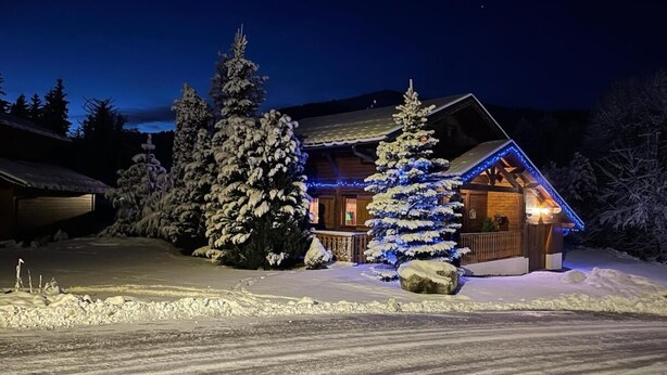 A snow-covered cabin with a wooden exterior, surrounded by snow-laden trees, and illuminated by blue lights. - Chalet, wifi, balcony, parking, tv, 90m², Les Gets (Les Gets)