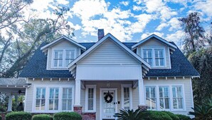 A two-story house with a front porch, a brick pathway leading to the entrance, and a clear blue sky with clouds.