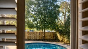 A view through a window of a backyard with a swimming pool, a wooden fence, and trees.