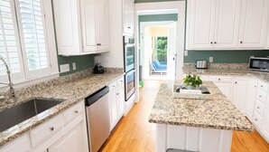 A kitchen with white cabinets, granite countertops, a ceiling fan, and a view to the outdoors.