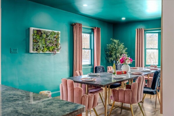 Comedor con paredes verde azulado, sillas rosas y una mesa dispuesta para cuatro.