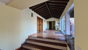 Un pasillo con una escalera de madera, un techo con una viga de madera oscura y una puerta con picaporte de metal.