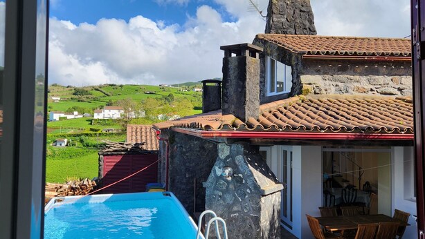 Una piscina con una escalera, una estructura de piedra y un área de comedor con sillas y una mesa.
