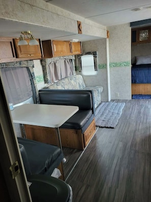 Interior compacto de uma caravana com cozinha compacta, sofá, mesa e janela.