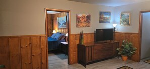 A room with wooden paneling, a bed with pillows, a TV on a wooden cabinet, and a potted plant. - The Hideaway on Locust, 2 bedroom, pet friendly home in Lead Hill, Arkansas (Lead Hill)