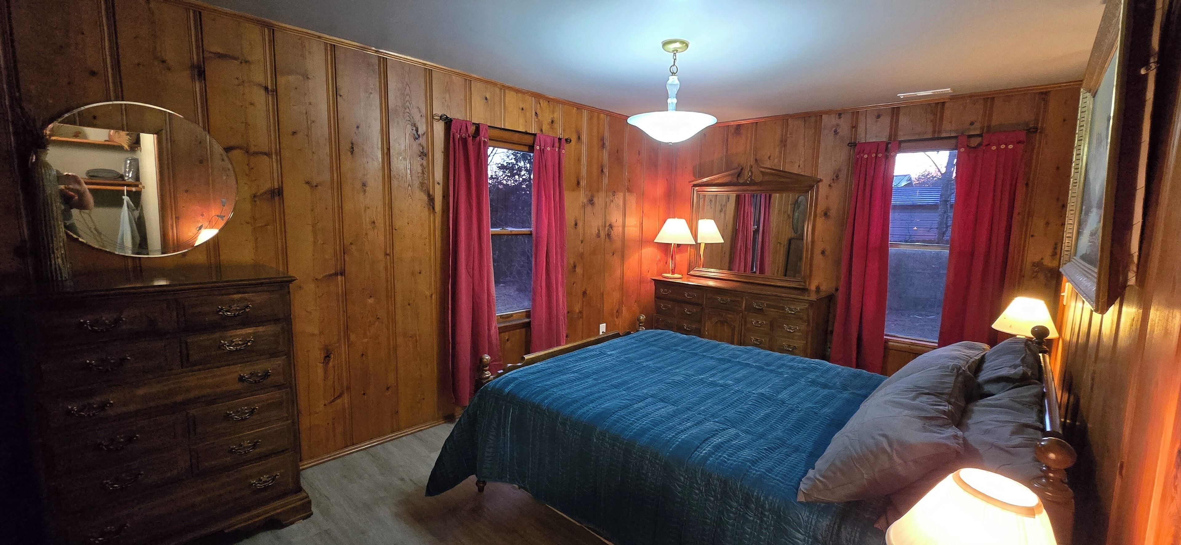 Un dormitorio con paneles de madera, una cama, un aparador y dos lámparas.