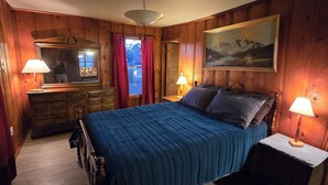 Une chambre à coucher aux murs lambrissés, avec un lit, deux lampes de chevet, une commode, un miroir et un tableau accroché au mur.