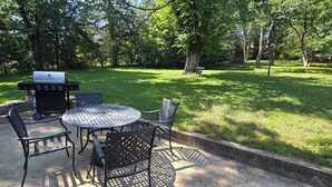Une terrasse extérieure avec un barbecue, des chaises en métal et une table ronde.