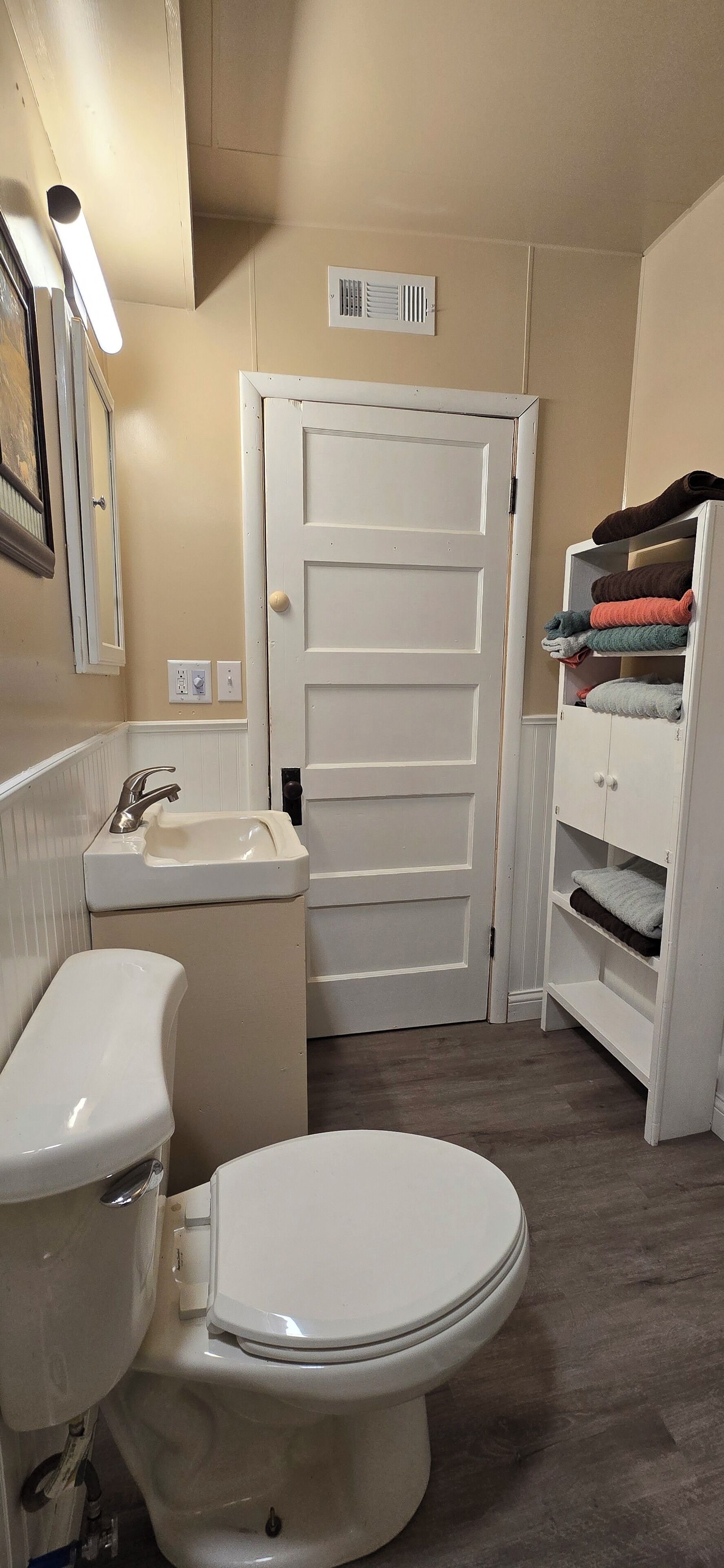 Une salle de bain avec des toilettes, un lavabo et une armoire blanche contenant des vêtements pliés.