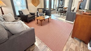 Een moderne woonkamer met een grijze bank, een houten salontafel en een vloerkleed met een visgraatpatroon.