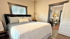 Een slaapkamer met een groot bed, een nachtkastje, een lamp en een raam met jaloezieën.