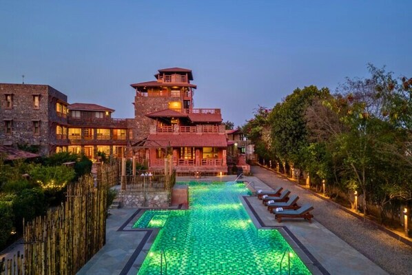A hotel with a pool, lounge chairs, and a stone building with a red roof. - Seraibagh Ranthambore (Sawai Madhopur)