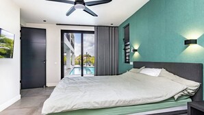 Ein modernes Schlafzimmer mit einem großen Bett, Deckenventilator, Blick auf einen Swimmingpool und einer grünen Wand.