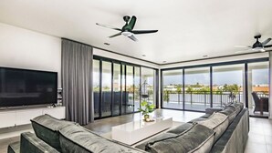 Ein modernes Wohnzimmer mit einem großen Flachbildfernseher, grauen Sofas, einem Couchtisch und einem Balkon mit Blick.