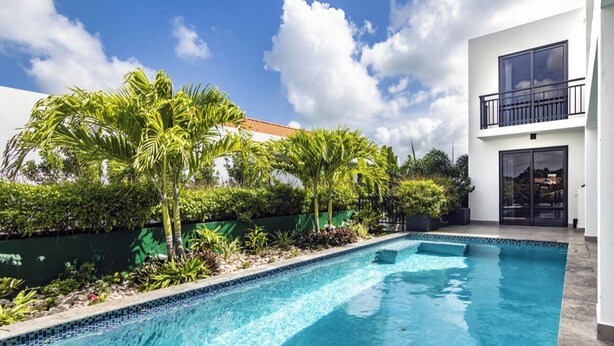 Ein moderner Poolbereich mit klarem, blauem Pool, umgeben von üppiger Vegetation und einem weißen Gebäude mit Balkon.