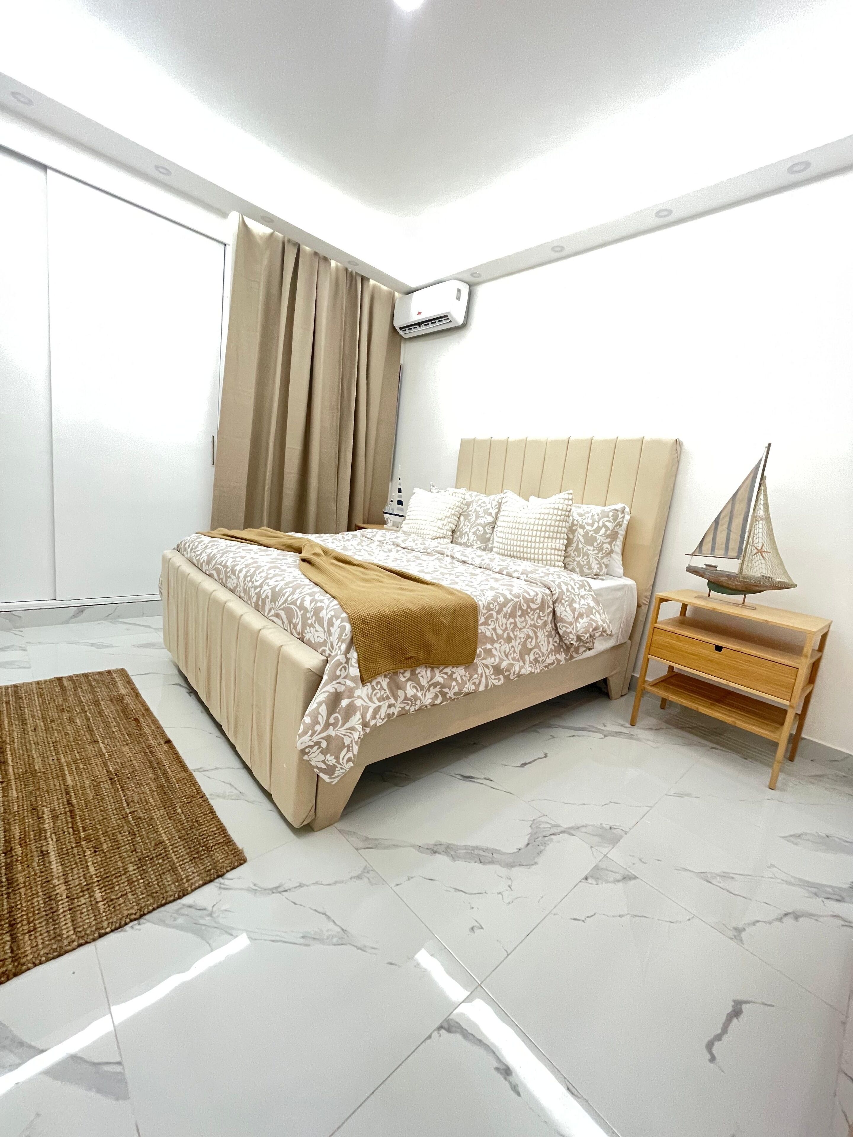 A bedroom with a bed, a nightstand, a small table, and a window with curtains.